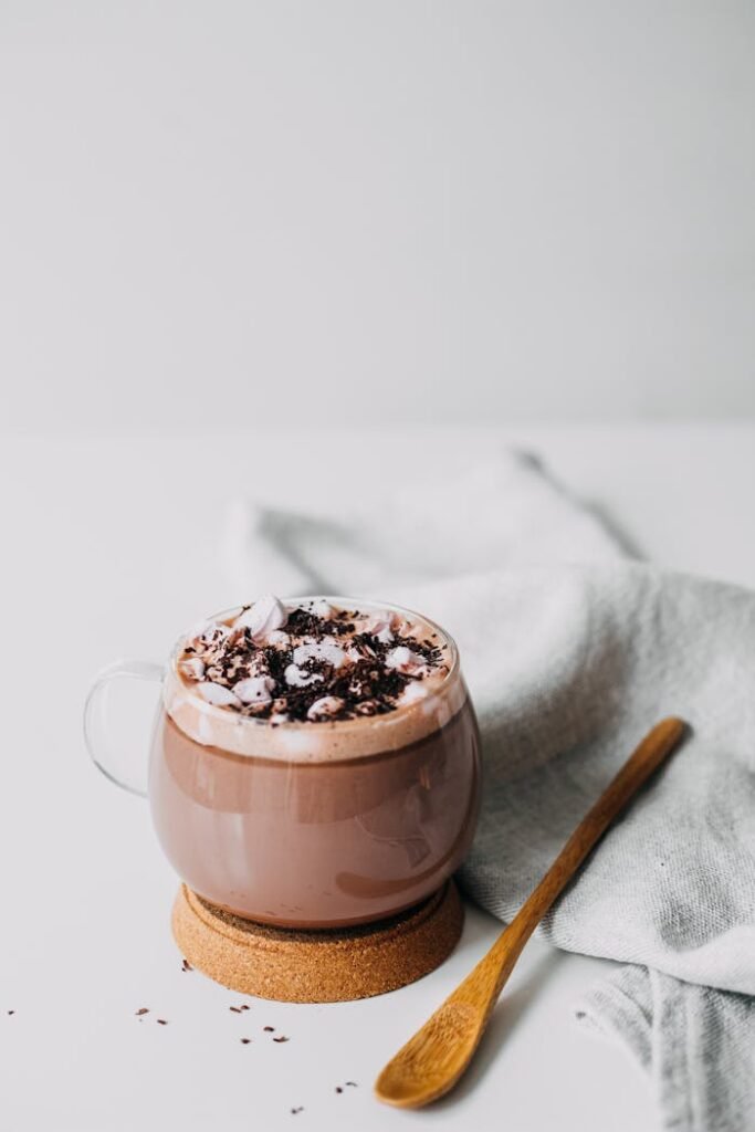 Delicious hot chocolate in a glass cup topped with marshmallows and cocoa, perfect for indulgence.